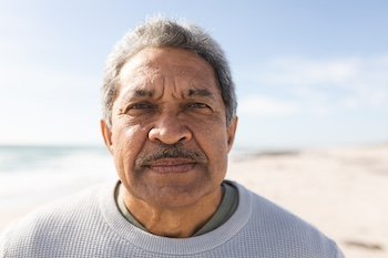 Close-up portrait of biracial senior man with mustache at beach against sky during sunny day. active lifestyle and weekend.